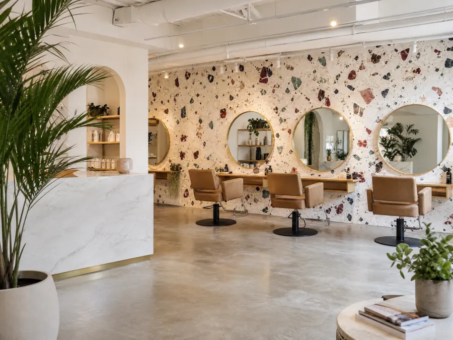 Cream terrazzo-pattern wallpaper with oxblood and teal speckles in a hair salon